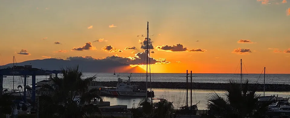 Denize batan güneş ve turuncu bulutlar, Kuşadası'nda marinadaki yelkenli direklerinin ardında
