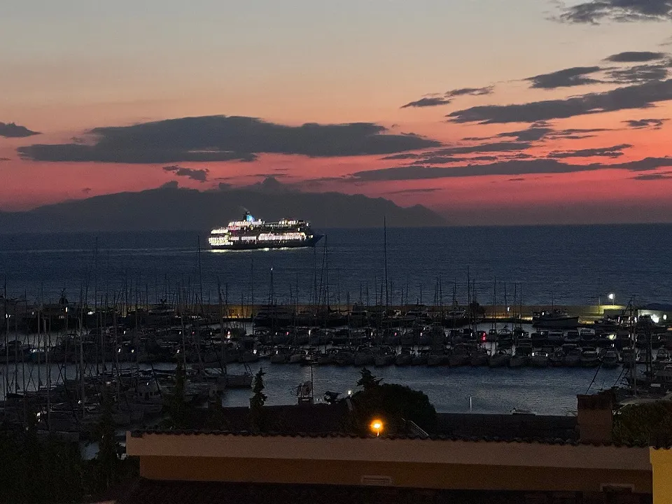 Işıklı kruvaziyer gemisi ve marinadaki yelkenliler, alacakaranlıkta pembe gökyüzü altında