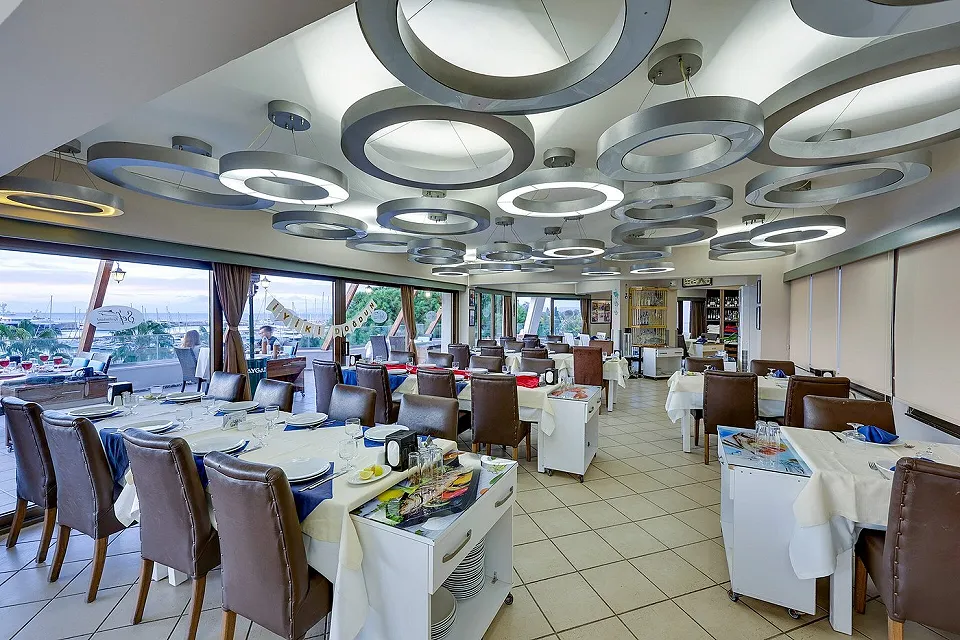 Halka lambalı geniş iç salon, beyaz örtülü masalar ve servis arabası, Şef Restaurant Kuşadası